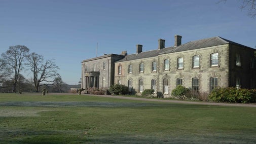 A lawn in front of a mansion with the blue sky and trees behind